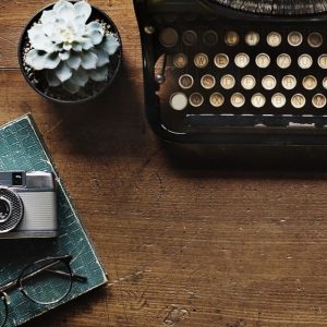 Old-fashioned typewriter with flower in mug and camera on book