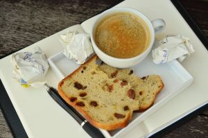 A writer's breakfast: coffee, raisin bread, and crumpled papers sit on a journal