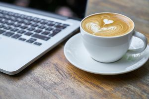 Frothy Coffee beside Laptop Keyboard